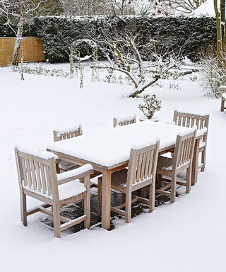 A snow covered backyard with a snow covered table and chairs