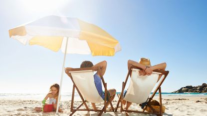 Family relaxing at the beach protected by a sun umbrella
