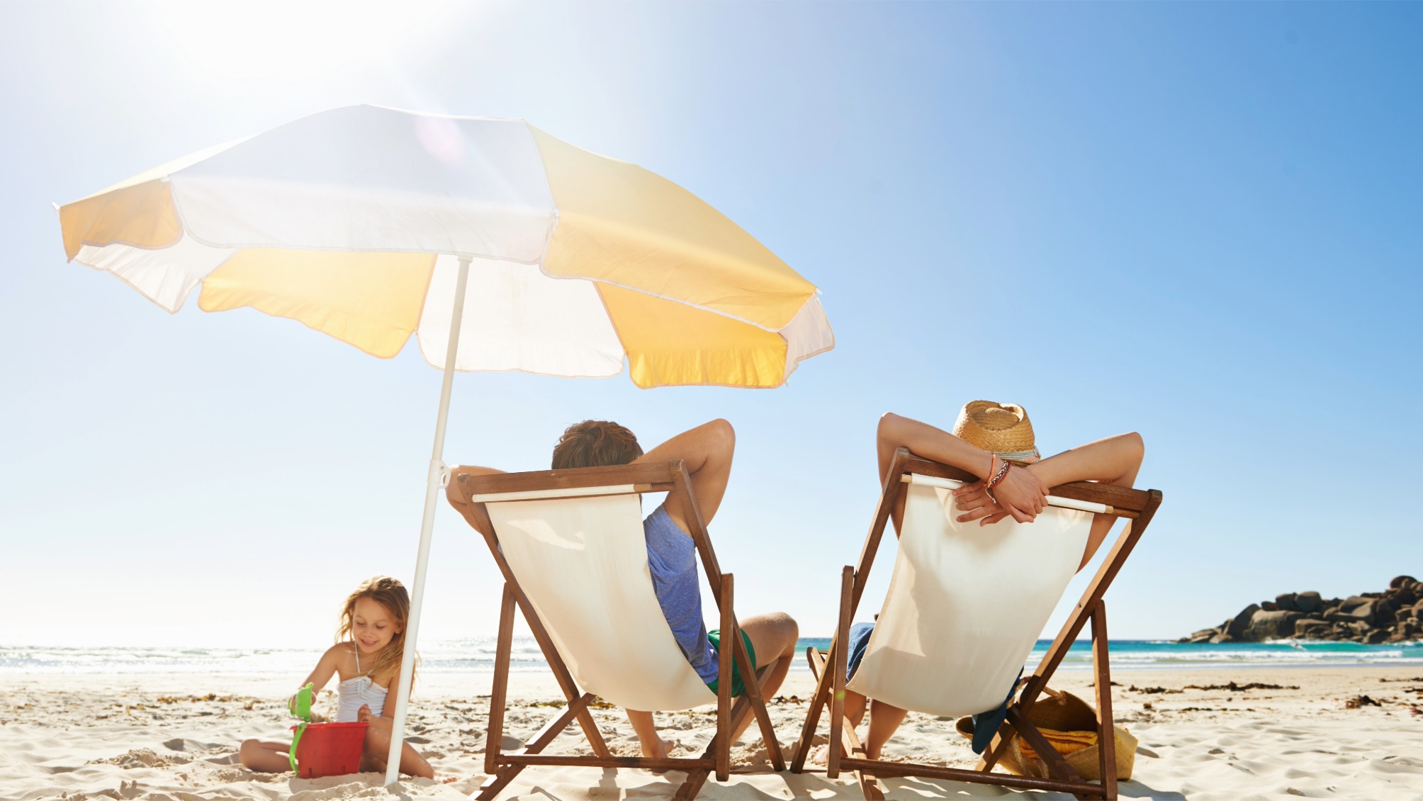 Family relaxing at the beach protected by a sun umbrella