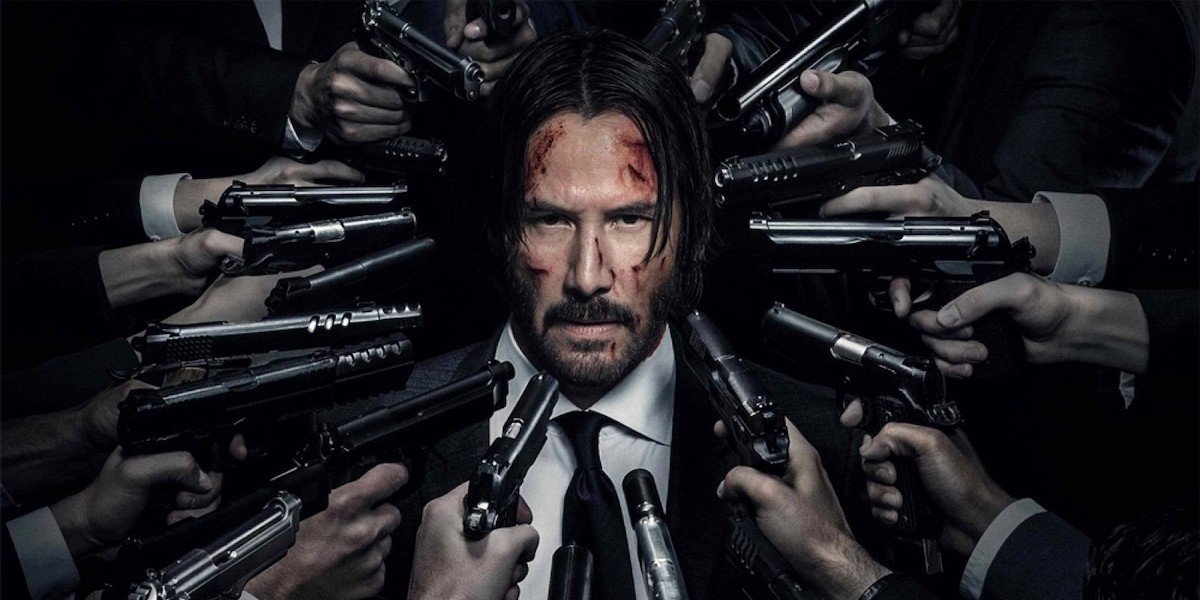 John Wick stands with a whole bunch of guns surrounding his head in a promotional image for the John