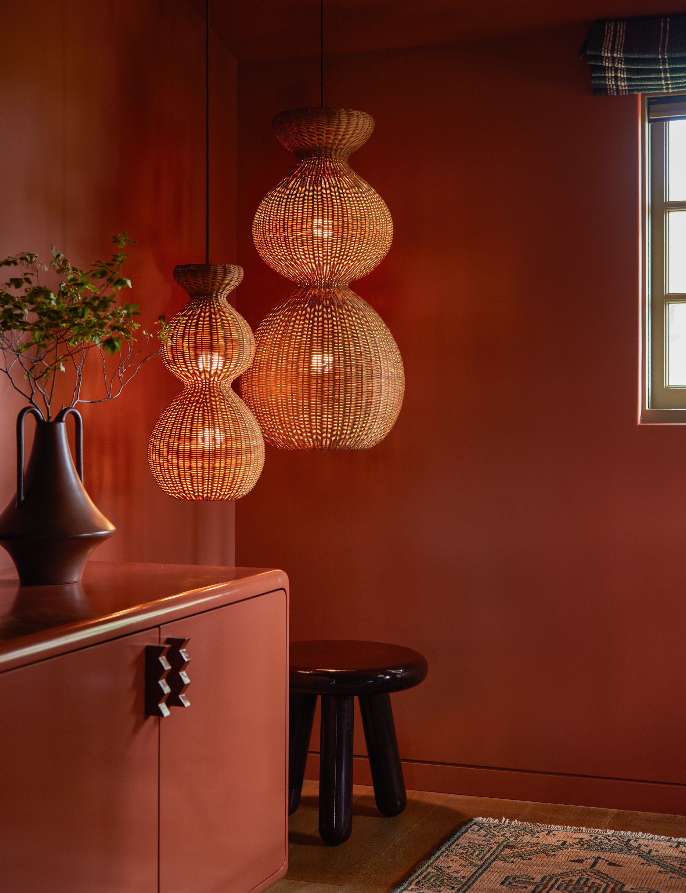 Terracota drenched room featuring a burgundy sculptural vase and two rattan pendant lights hanging in the corner