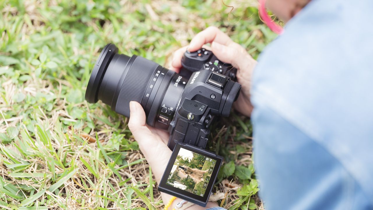 Nikon Z5 II camera in the hand at ground level, touchscreen flipped out and angled up