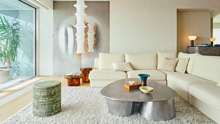 Living room with cream textured walls, cream corner sofa, aluminium coffee table, green stool, amber glass side tables and white paper pendant lights