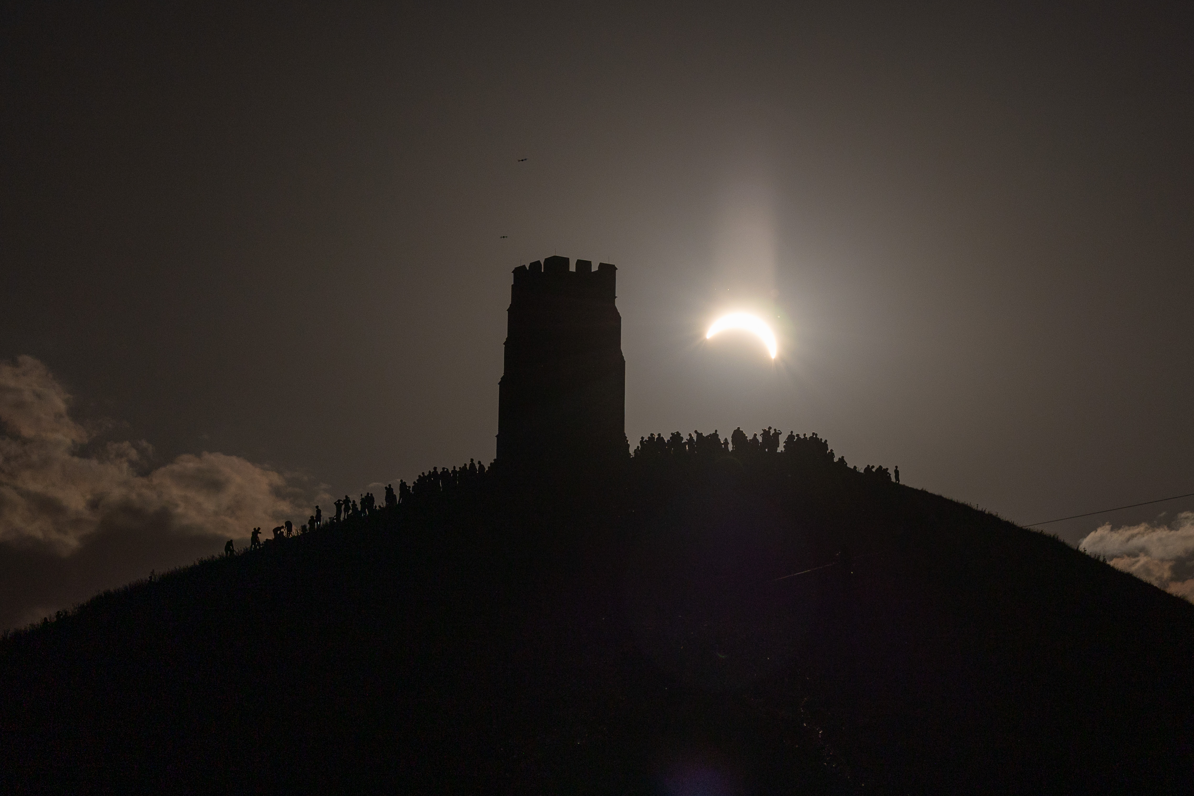 GLASTONBURY, ENGLAND - AUGUST 12: People view the partial solar eclipse besides the historic St. Michael&amp;amp;apos;s Church tower, a Grade I listed building at the top of Glastonbury Tor on August 12, 2026 in Glastonbury, England. The partial solar eclipse is the most coverage during an eclipse viewed from the UK since 1999, with the moon covering 90-96% of the sun. (Photo by Matt Cardy/Getty Images)