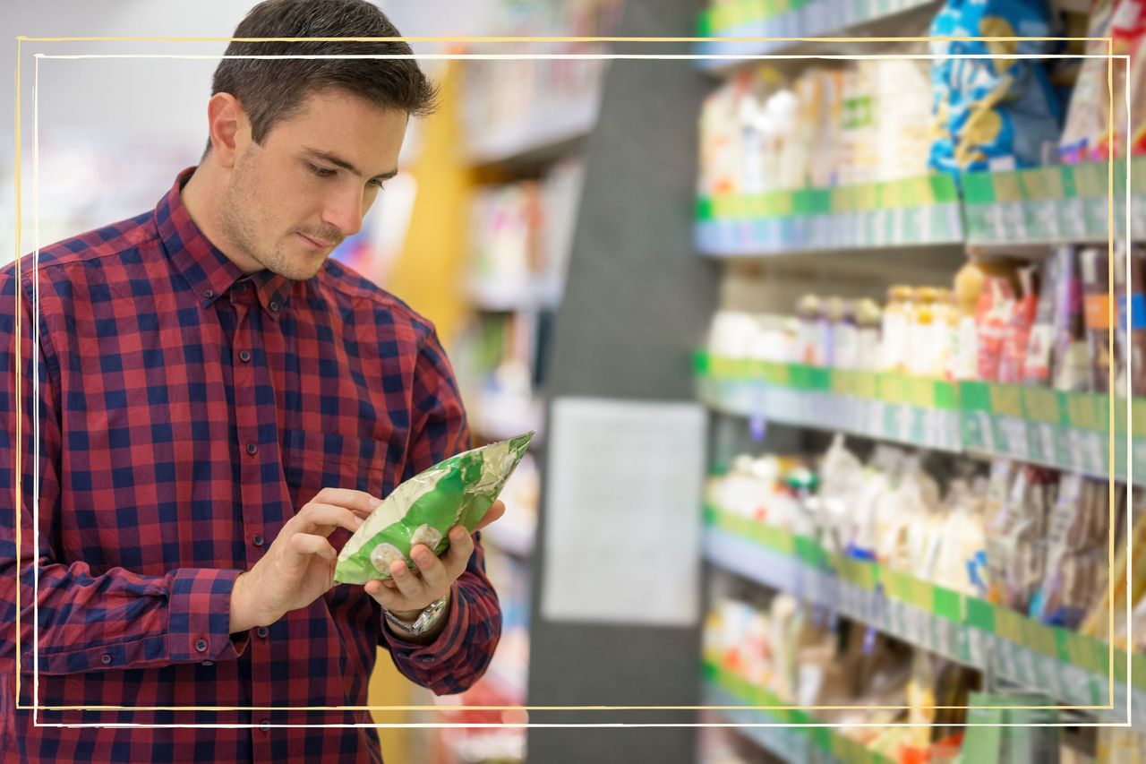 A man in a supermarket aisle looking at the ingredients on the back of a packet of Lentil Chips