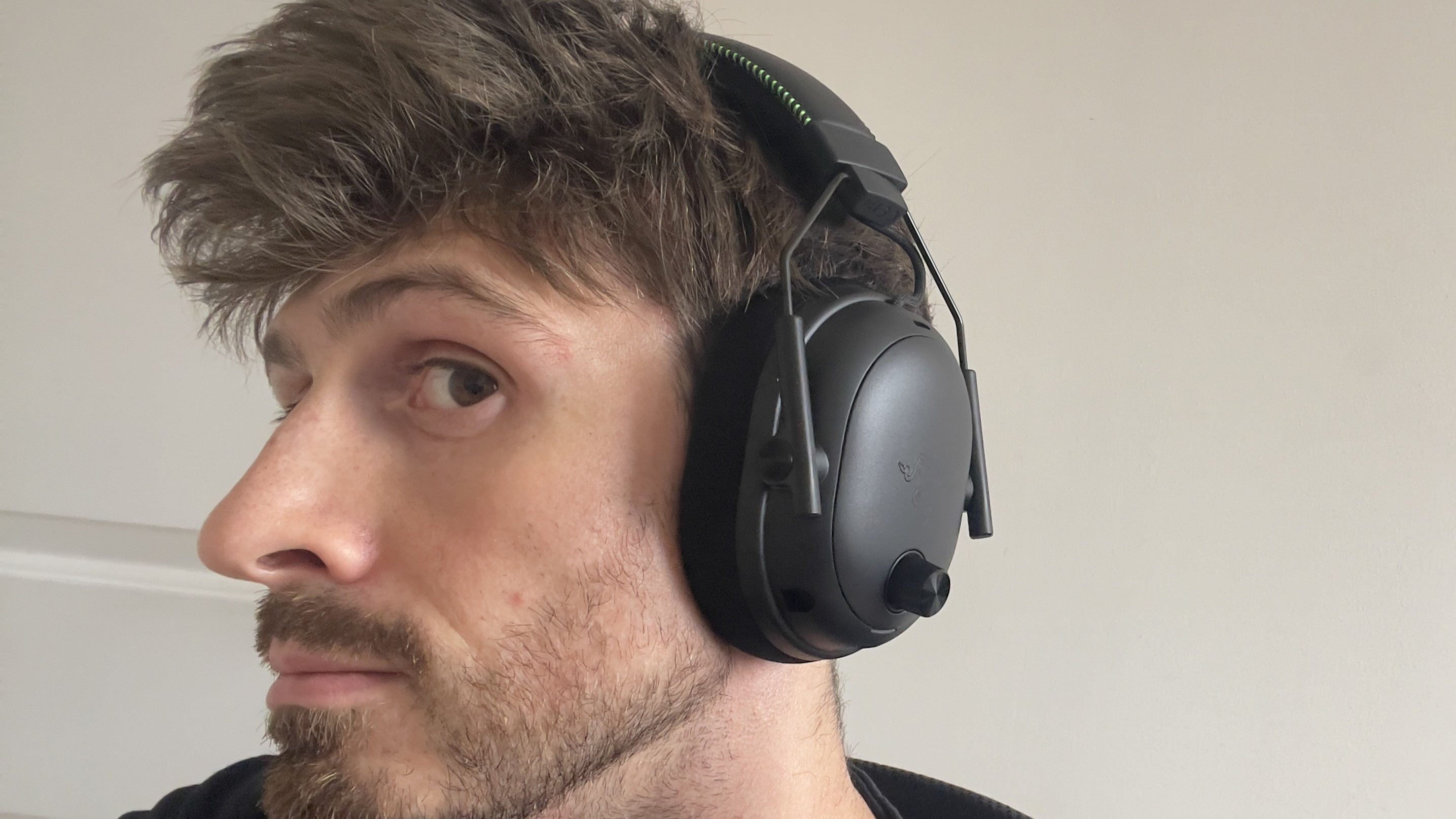 The Razer BlackShark V3 Pro headset being worn by a mann its box on a desk