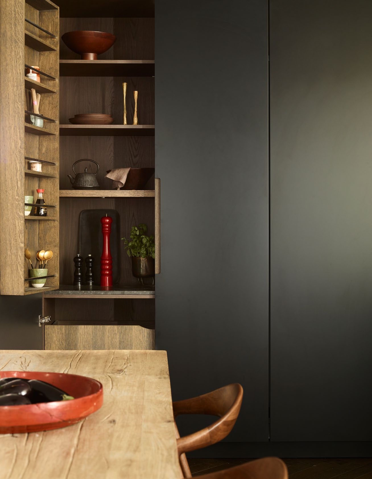 Black kitchen cabinets with one door open to show interior shelves in dark wood stocked with various cooking equipment