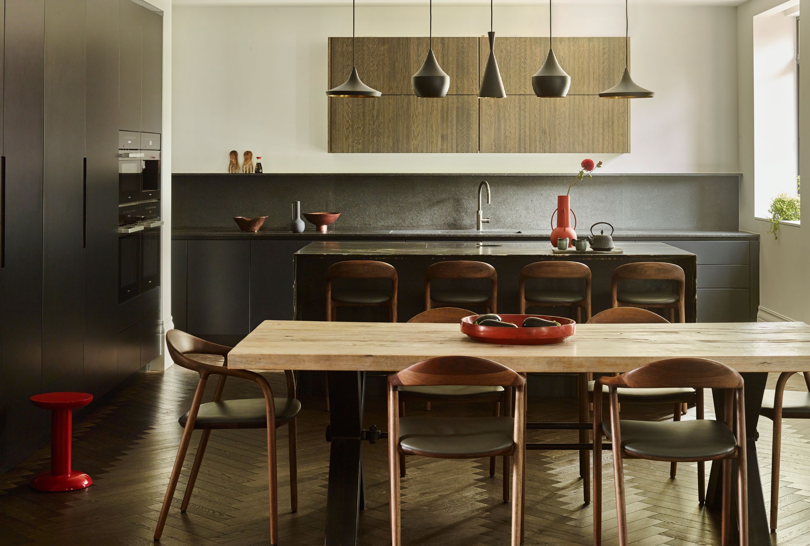 black kitchen with white walls, light wood kitchen table and matching dark wood bar stall and dining chairs with dark green seat cushion
