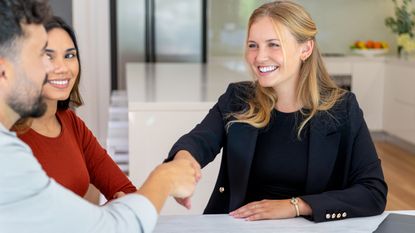 A financial adviser shakes hands with a client as a couple meet with her in her office.