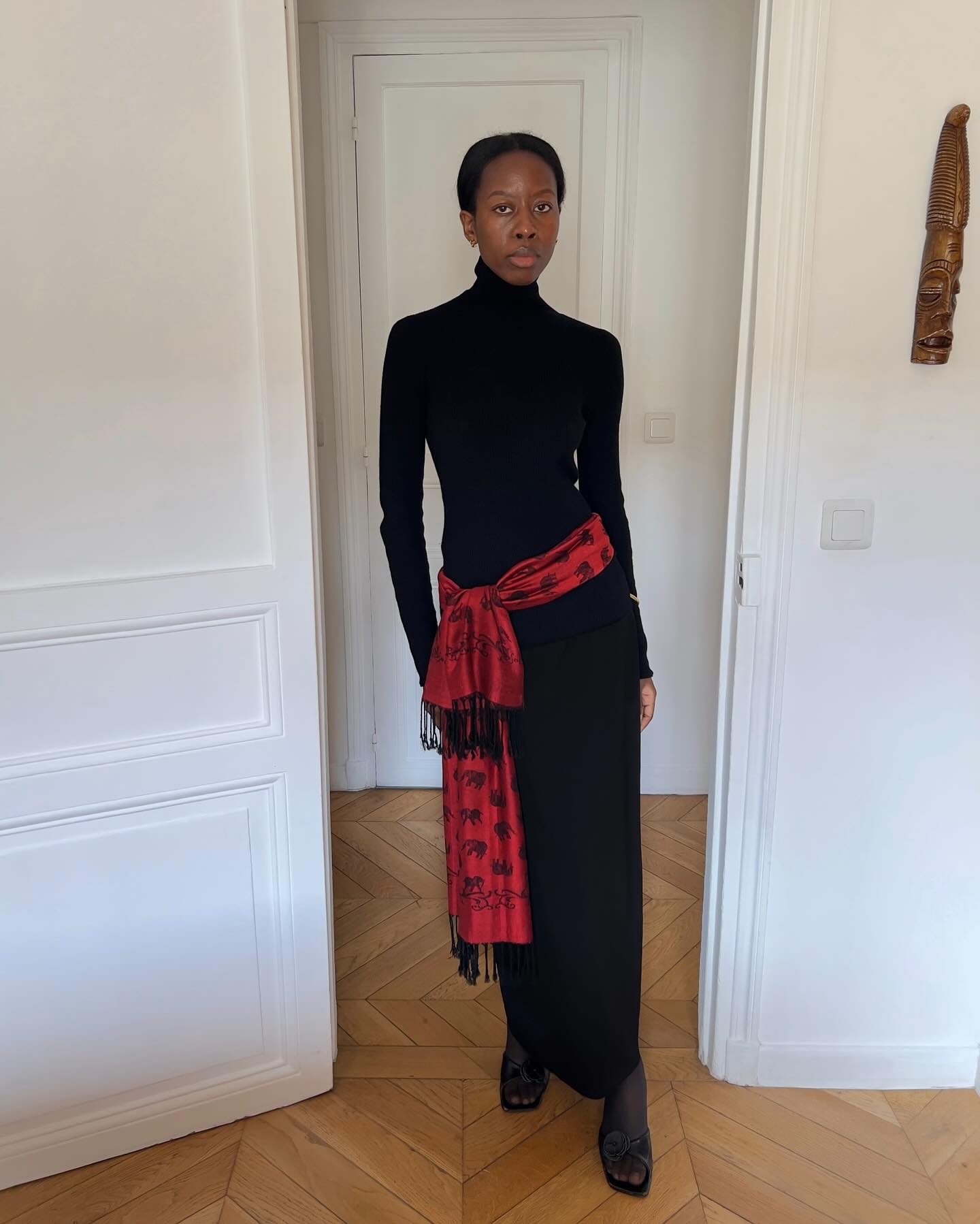 @sylviemus_ wearing a black turtleneck dress with a red long scarf with fringe.