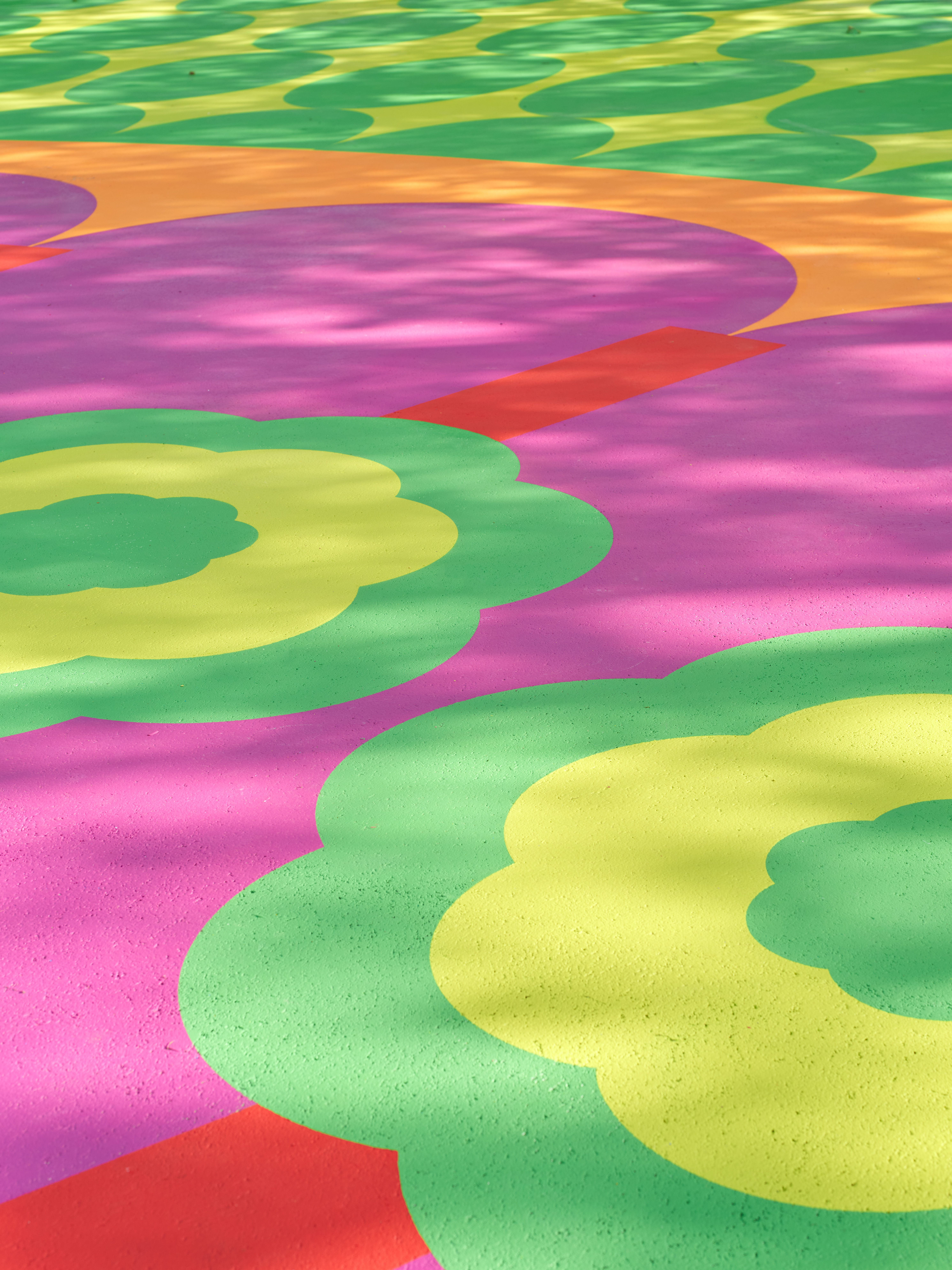 Aerial view of a colorful, abstract mural in tones of pink, red, green, yellow, and blue as seen up close on a sunny day.