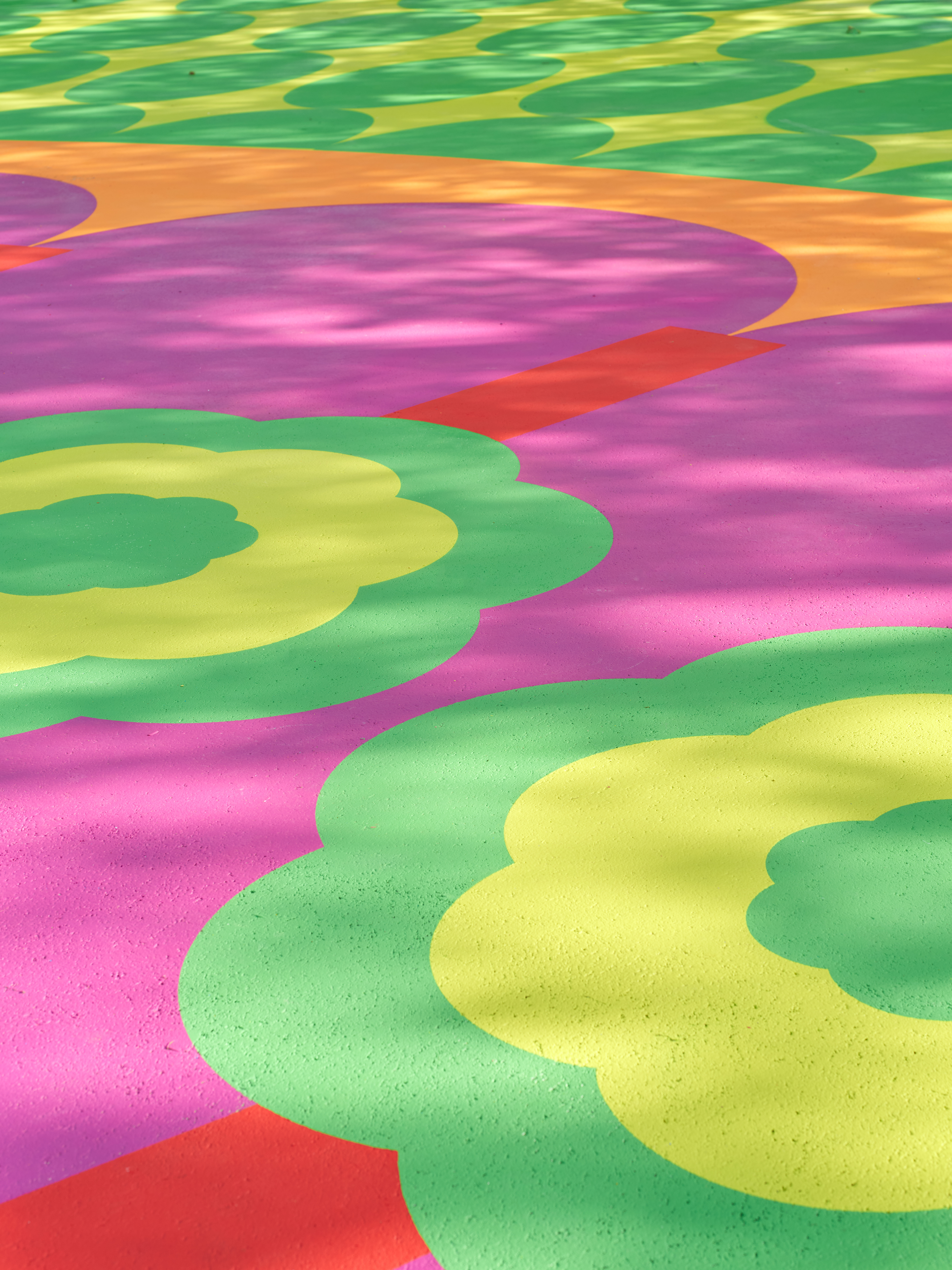 Aerial view of a colorful, abstract mural in tones of pink, red, green, yellow, and blue as seen up close on a sunny day.