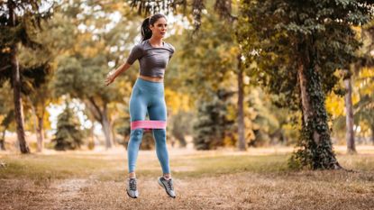 Woman performs a jump squat wearing a resistance band 