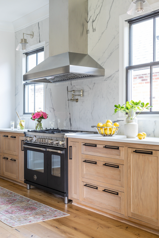 A kitchen with wooden cabinetry, a large range oven, wooden floors and marble walls