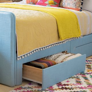 divan bed upholstered in blue fabric with concealed drawers in the base for added storage