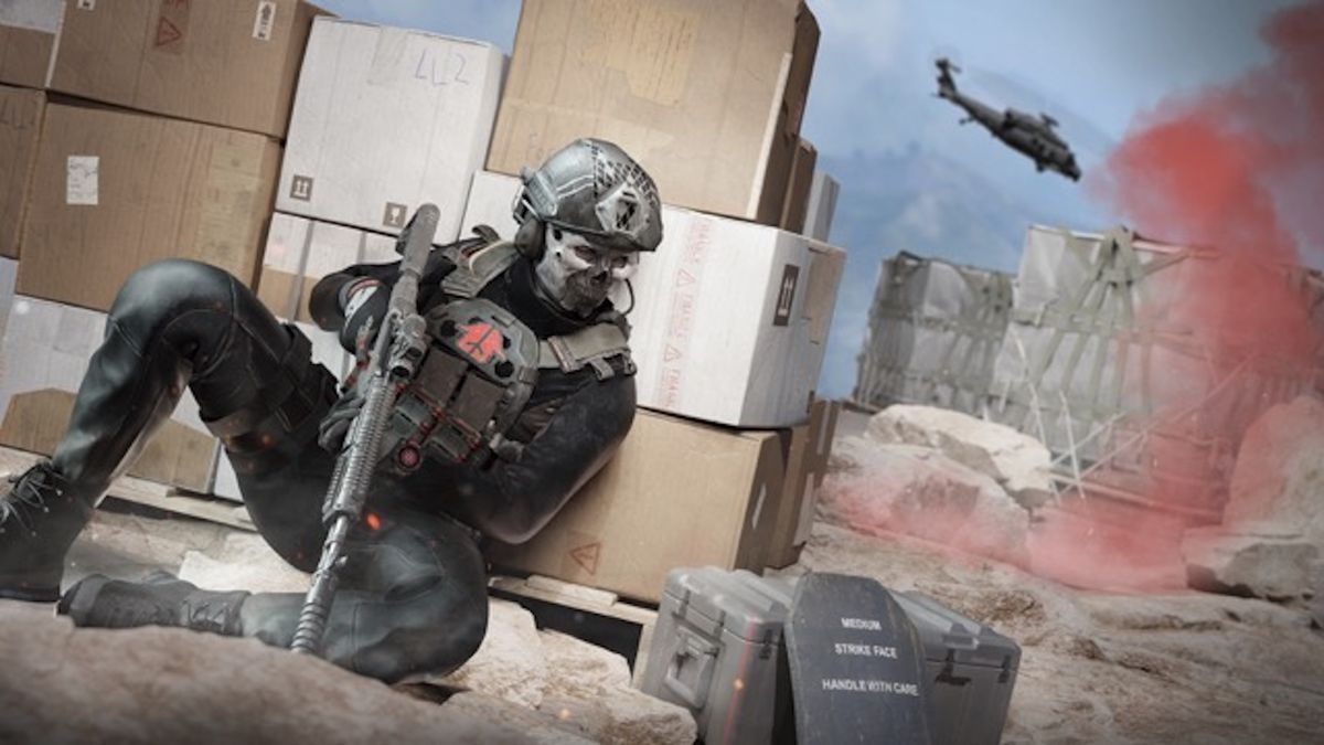 A soldier crouching behind cover as a helicopter flies over red smoke markers in the distance