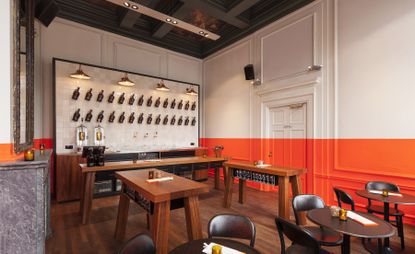 Bar with lower-half of walls in vibrant orange. Dark wood tables and chairs