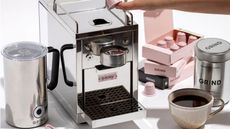 Grind One Pod Machine on a countertop with pods, a cup of coffee, and a milk frother around it