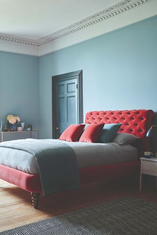 blue bedroom with red bed and cushions, blue painted door, wooden floorboards, rug