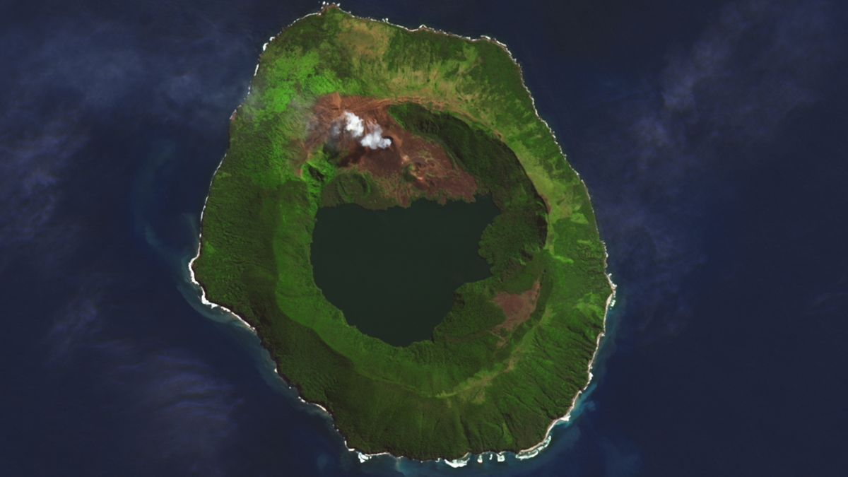 A satellite photo of an island with a massive caldera and crater lake with smoke coming from part of the volcano