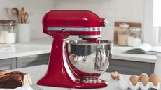 An Empire Red KitchenAid stand mixer next to a cinnamon swirl cake and broken eggs 