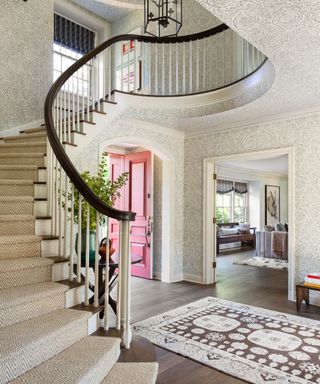 hall with patterned wallpaper curved stairs and brick red front door open