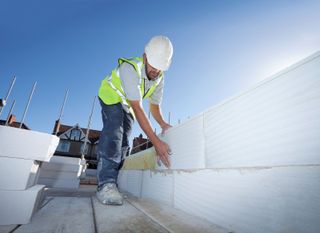 Building materials prices on a housebuilding site with a builder in a high-vis jacket and jeans moving building blocks