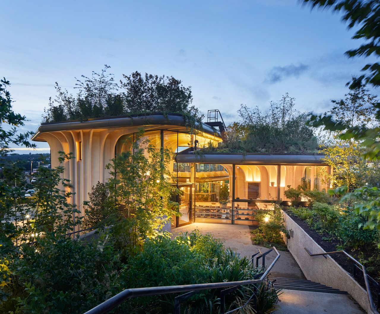 Exterior of the Maggie&#039;s Centre with a walkway through greenery