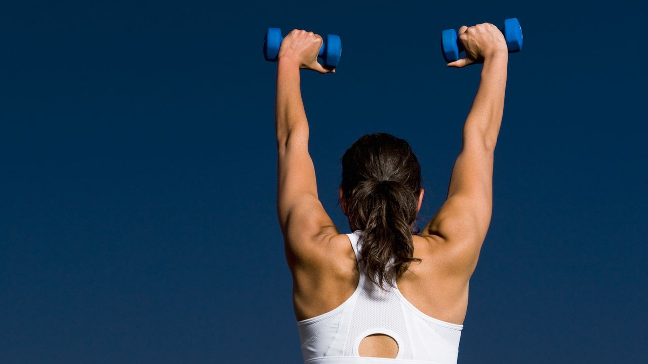 The back of a woman lifting dumbbells above her head