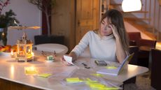 A woman looks a bit stressed while working on financial paperwork at her kitchen table.