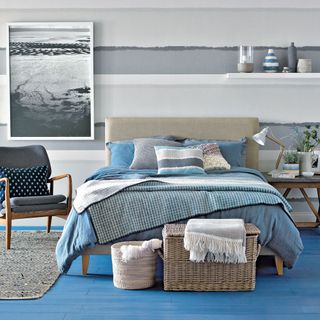 bedroom with grey and white wall blue wooden flooring and grey bed with blue cushions