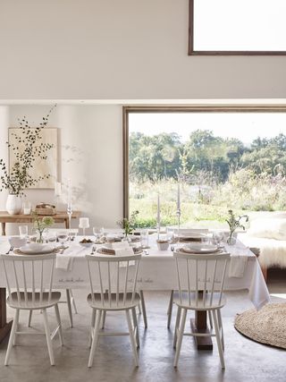 dining room with large glazed window, white walls with dining table, chairs and white table dressings