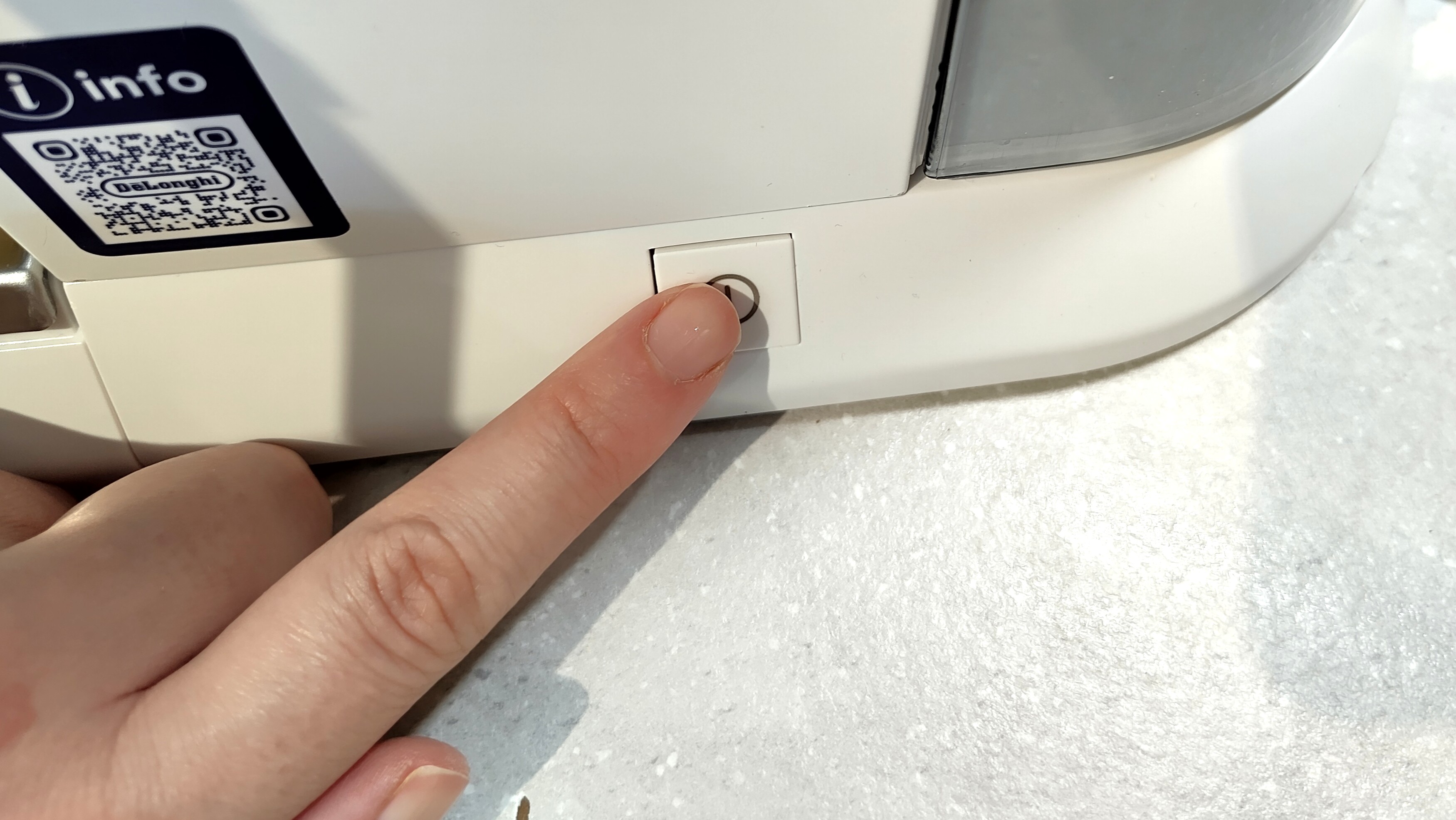 Person's hand pressing power button on De'Longhi Dedica Duo espresso machine