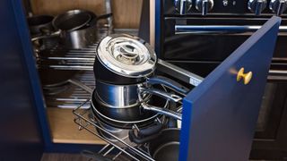 A blue kitchen cupboard with built in pull out storage containing pots and pans 