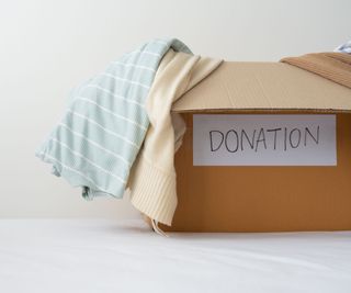 A cardboard box with a donation label on the front, a blue and white shirt overhanging the edges