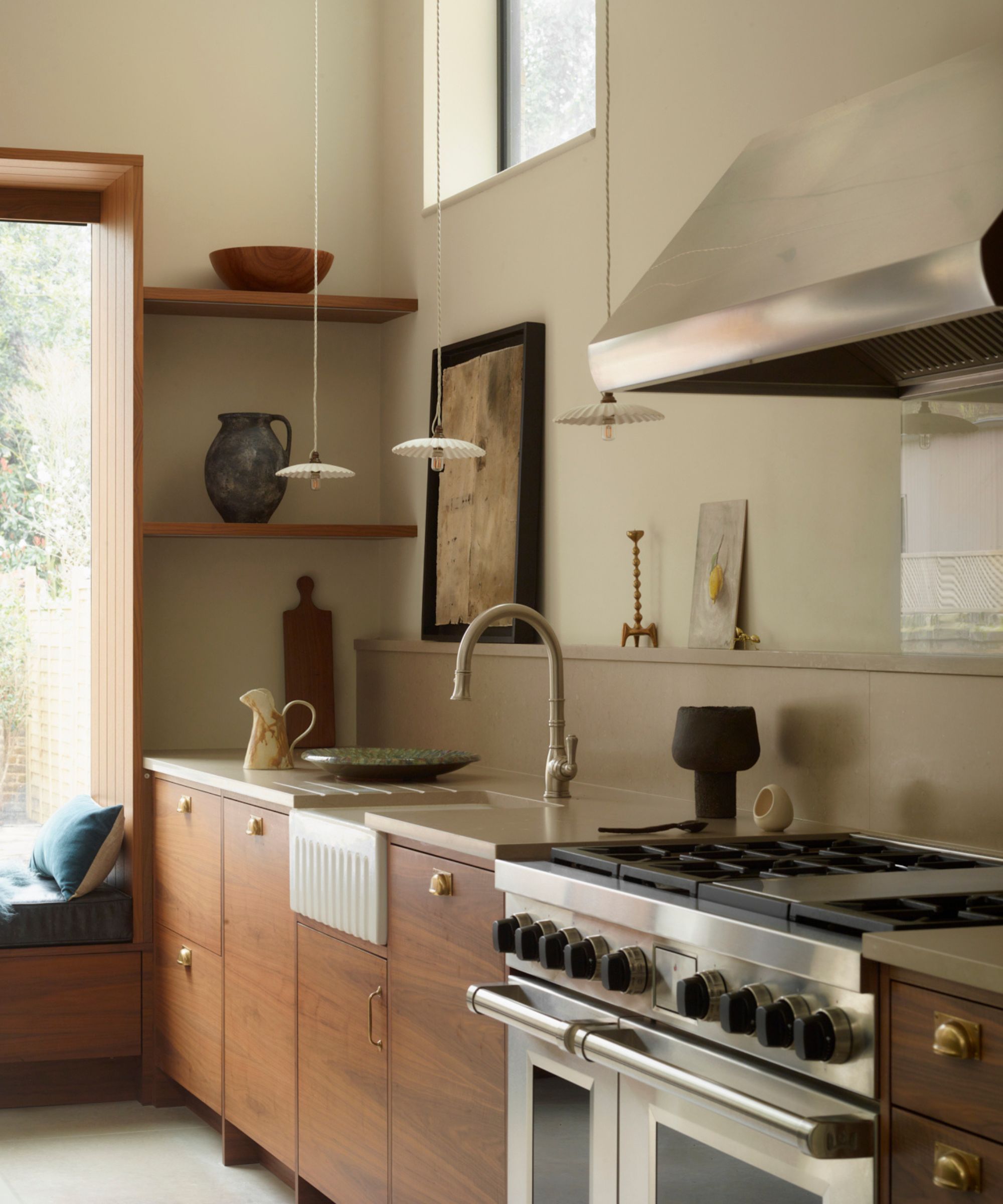A one-wall kitchen with wooden cabinets, stainless steel appliances, white walls, and open shelving displaying art