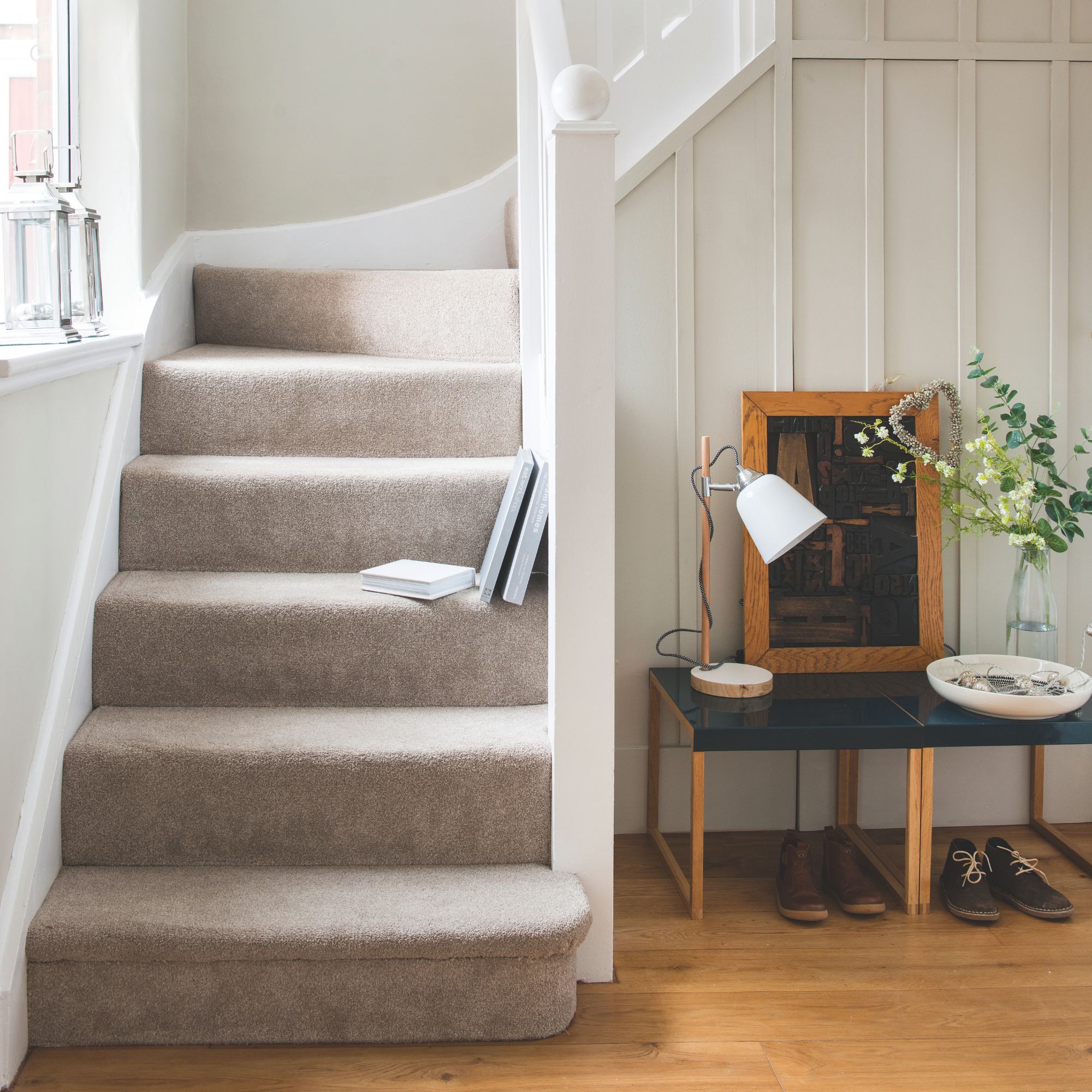 Brown carpeted stairs in a hallway with wooden flooring and a little console table next to it