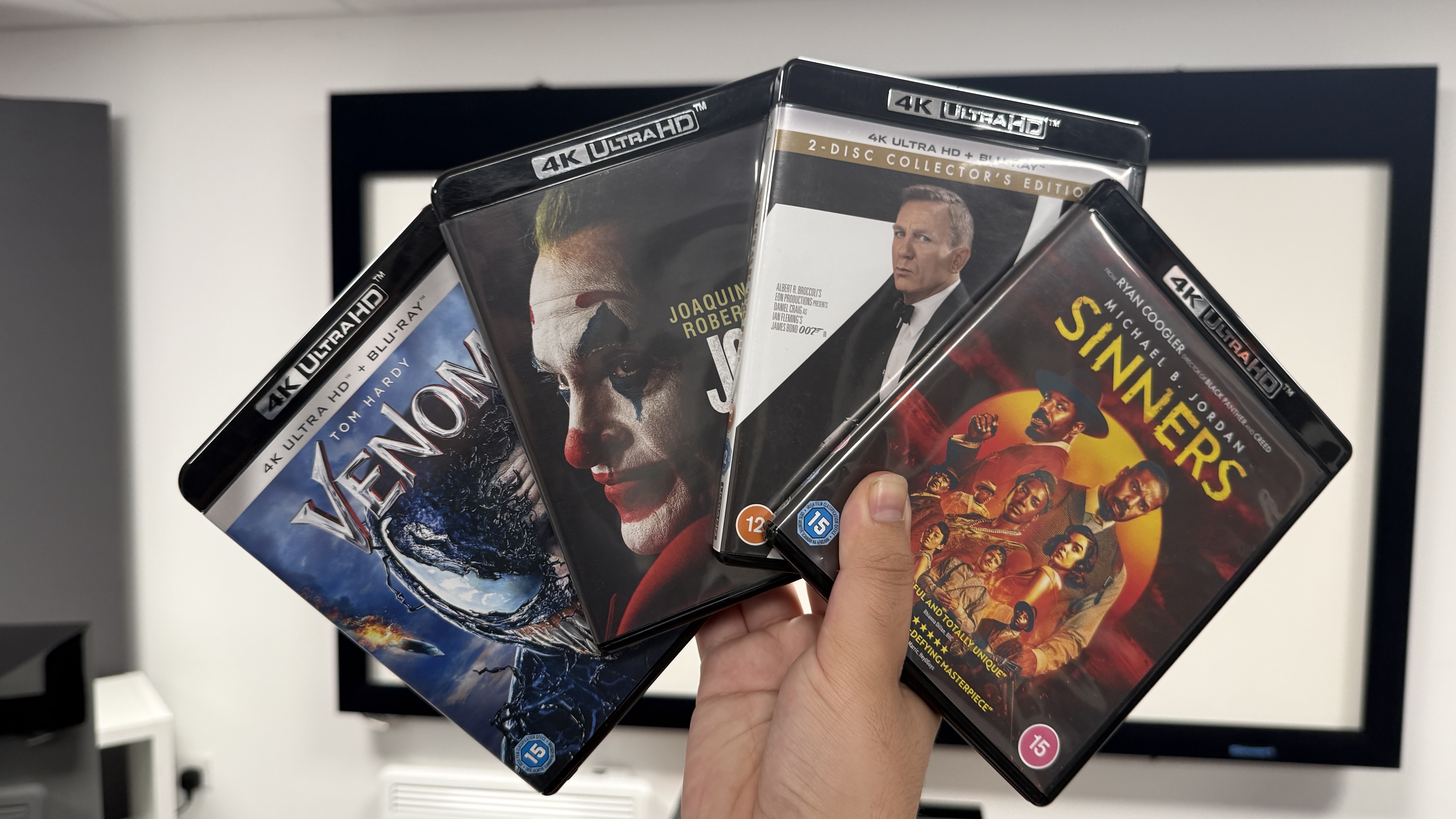 A hand holds four 4K Blu-ray disc cases in a fan orientation
