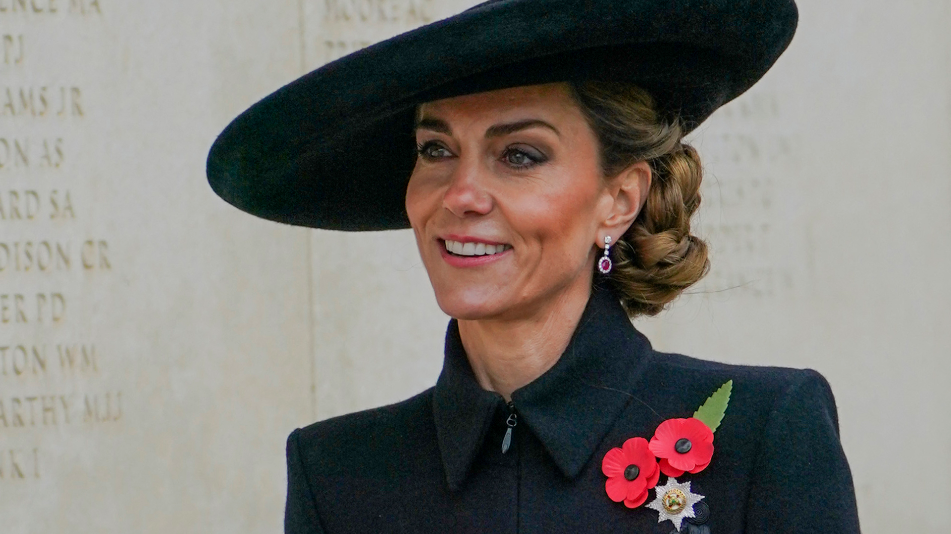 Kate Middleton wearing a black coat and hat and poppy pins