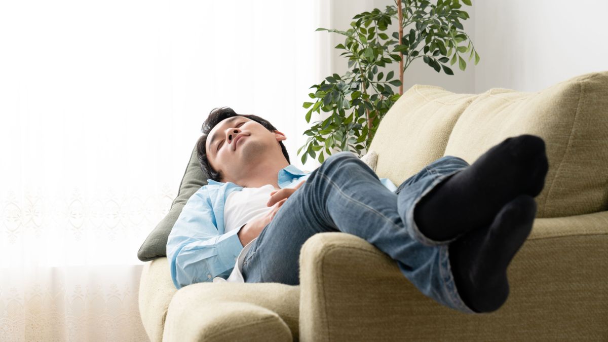 The Navy SEAL Sleep Technique: a man with dark hair naps on a sofa with his legs elevated