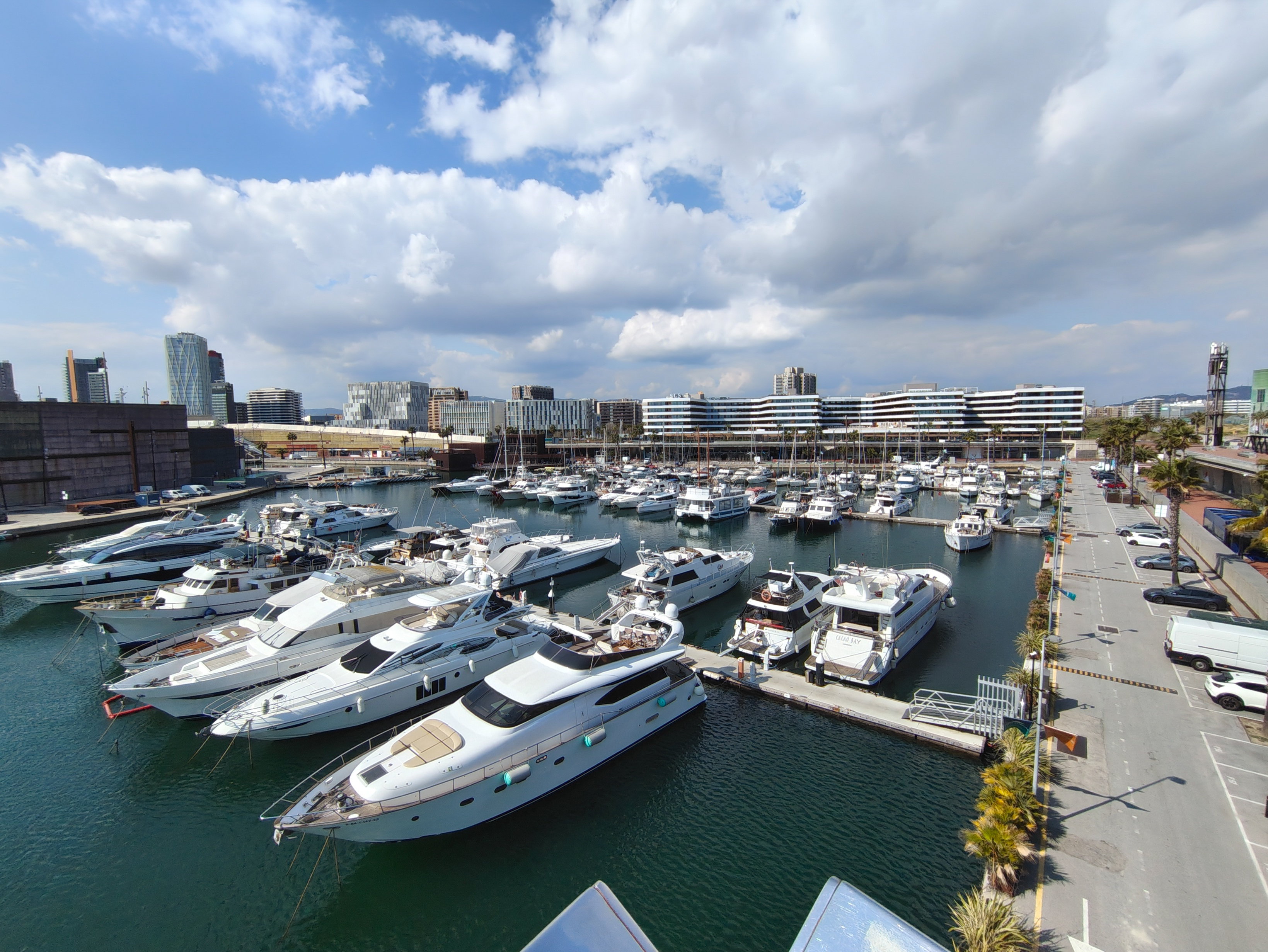 Wide photo of a marina filled with yachts and boats under a partly cloudy sky in Barcelona, captured with the Nothing Phone (4a).