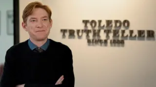 Domnhall Gleeson stands in front of a sign for the Toledo Truth Teller newspaper