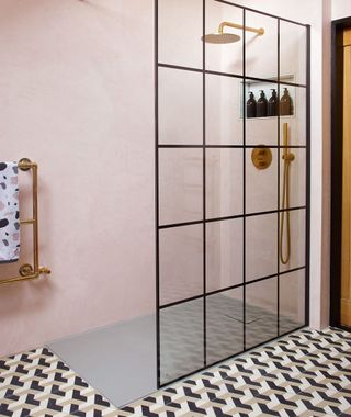 bathroom with blush pink walls, geometric floor tiles, large walk-in shower with glass pane divider with black trimming, and gold chrome towel rail and tap fixings