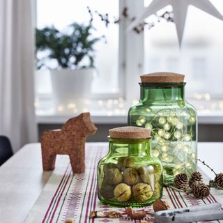 Christmas table runner with stripes and stars, two jars with walnuts and fairy lights, Scandi horse