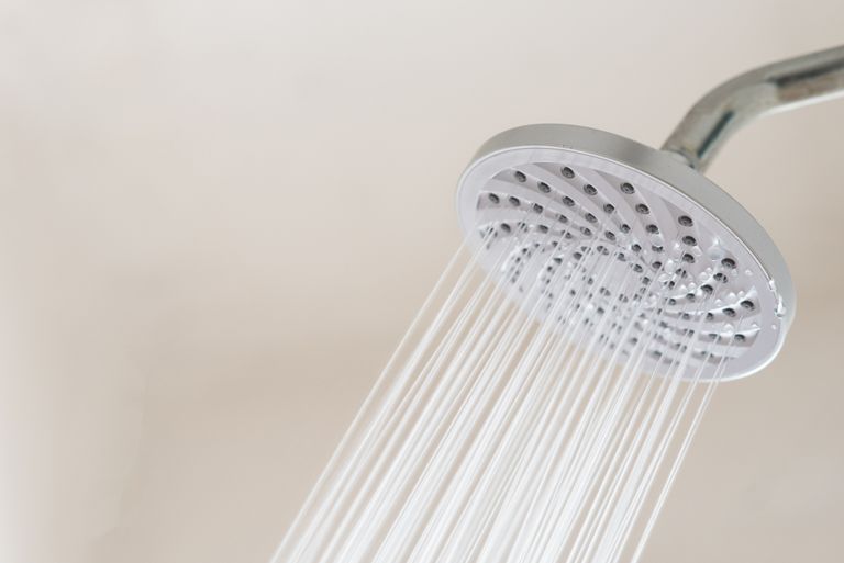 Close up of a chrome showerhead spraying water on a pale pink background