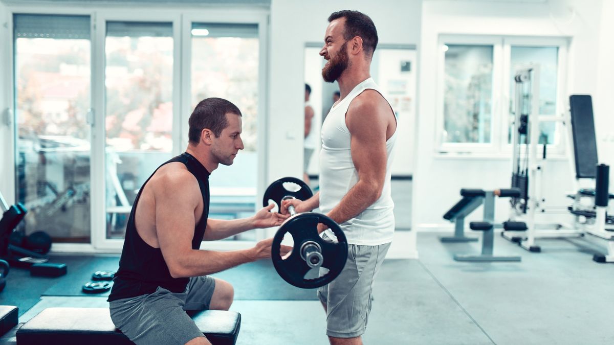 Coach helps client with barbell curl