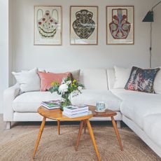 A white living room with a white corner sofa and vintage nesting tables with a vase of flowers on top