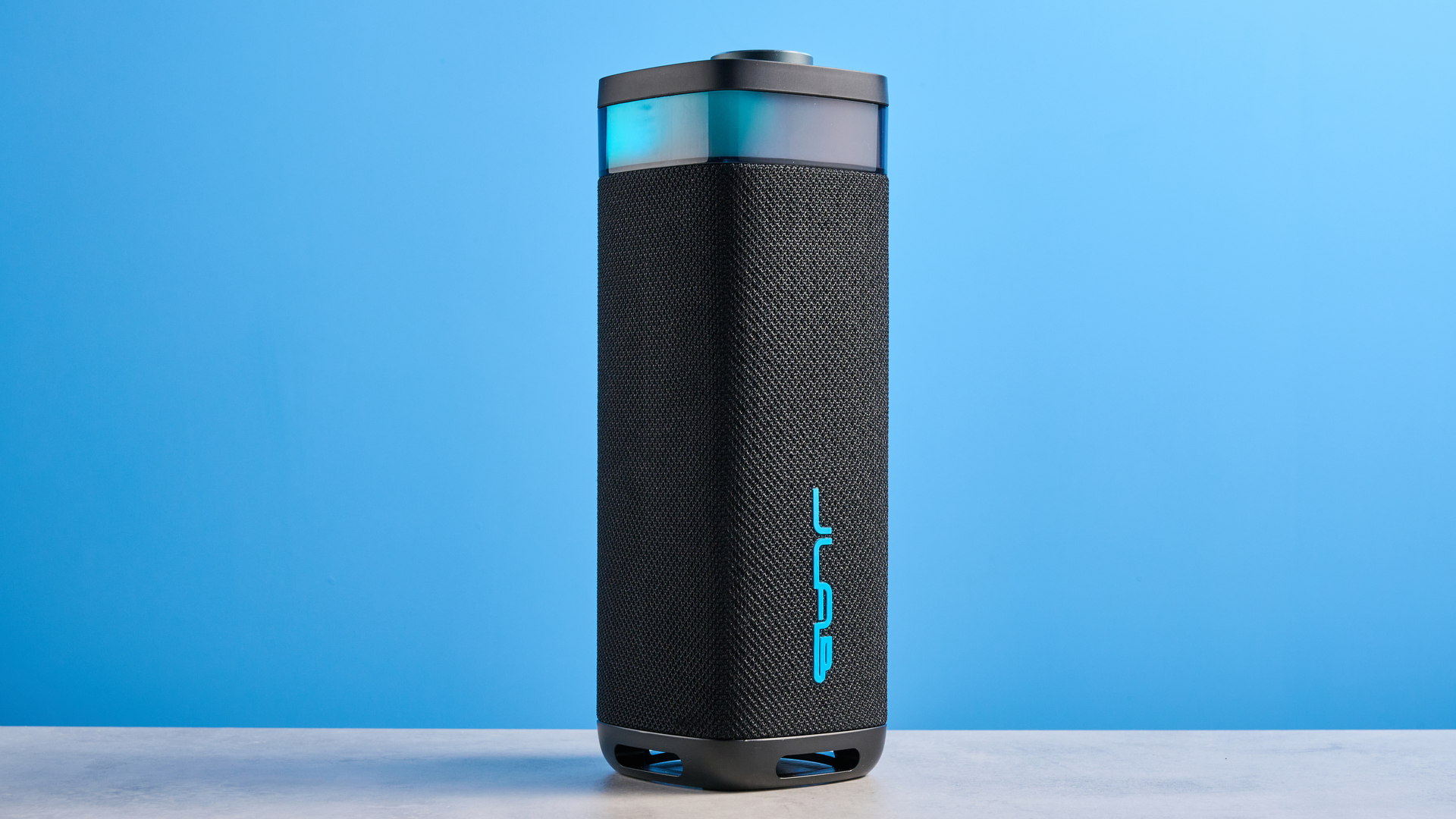 the jlab jbuds party speaker with LED rainbow lights photographed against a blue background