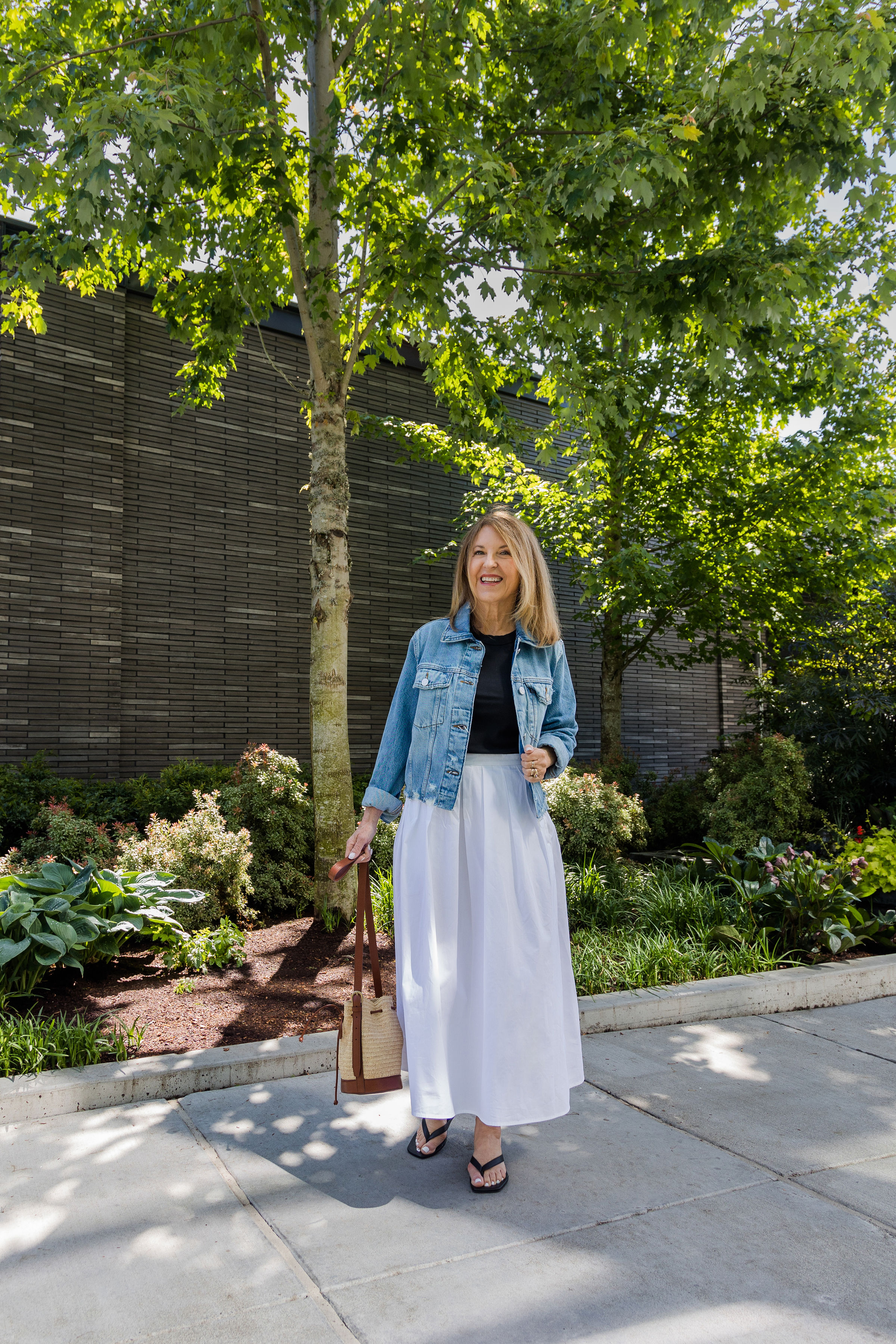A former VIP Nordstrom stylist wearing a jean jacket over a black top, a white midi skirt, and flip-flops.