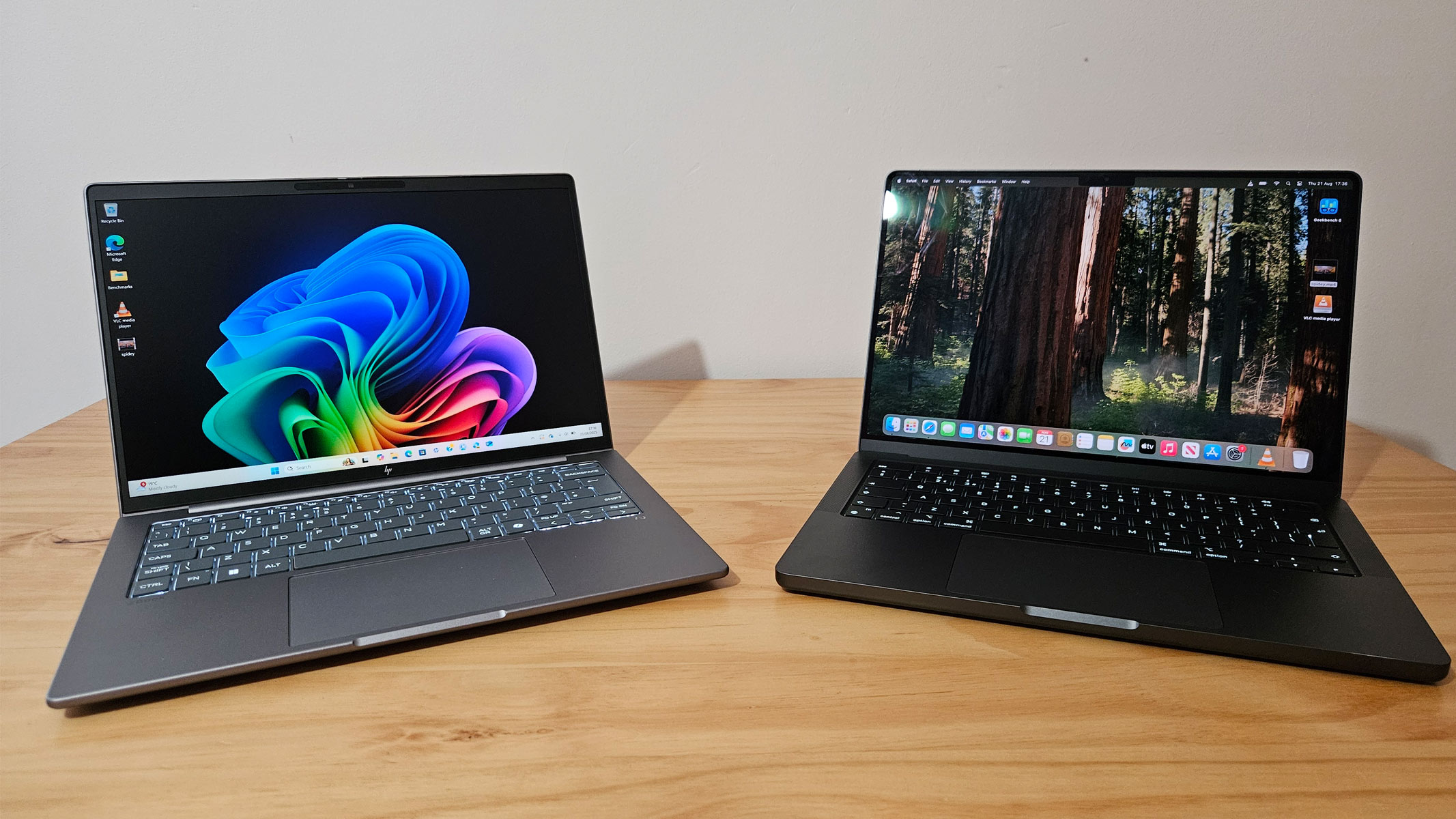 A Windows laptop and MacBook opened next to each other on a wooden table.